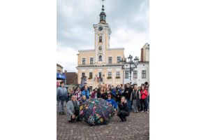 Grupa uczestników akcji artystycznej pozuje wokół pomalowanego parasola na rynku w Skoczowie.