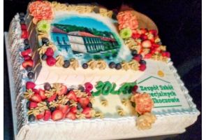 Tort jubileuszowy z okazji 30-lecia szkoły, ozdobiony owocami i zdjęciem budynku szkoły.