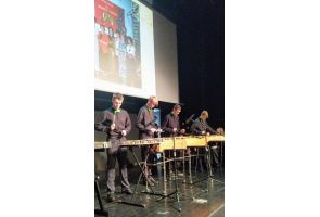 Grupa uczniów gra instrumentach perkusyjnych na scenie podczas uroczystości szkolnej.